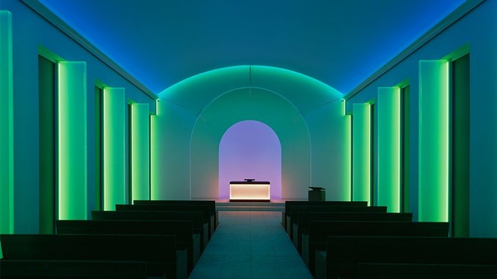 Modern Kirche mit blauer und grüner Beleuchtung, Holzbänken und einem Altar am Ende.