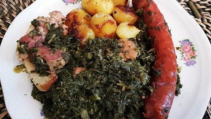 Das Bild zeigt ein Gericht mit Fleisch, Kartoffeln, Wurst und Grünkohl