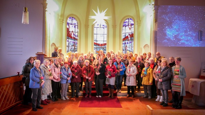Eine große Gruppe Menschen steht unter einem Herrnhuter Stern im Altarraum einer Kirche. Alle Halten eine rote Rose.