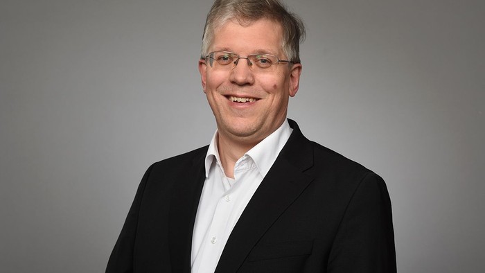 Mittelalter Mann mit Brille, der einen schwarzen Blazer und ein weißes Hemd trägt.