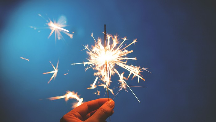Eine Hand hält ein brennendes Feuerwerk vor blauem Himmel
