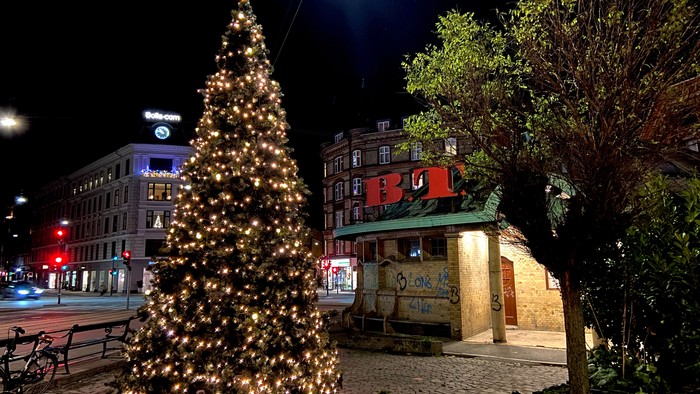 Juletræ pyntet med lys, der oplyser en festlig byplads om natten.