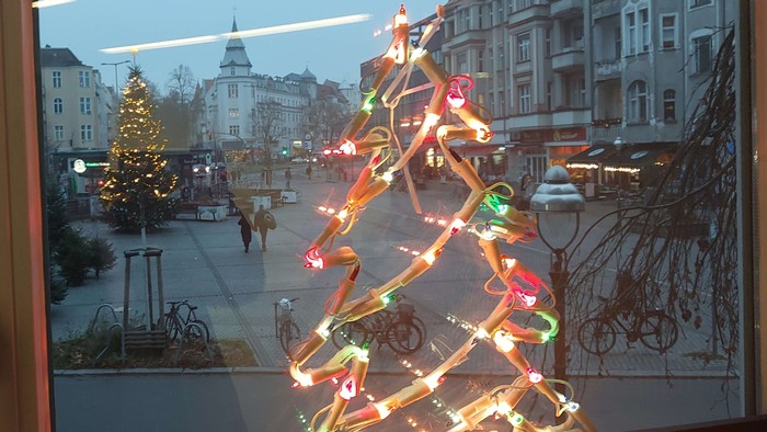 Ein Neon-Weihnachtsbaum leuchtet am Fenster, das auf einen Platz - den Breslauer Platz in Friedenau - zeigt