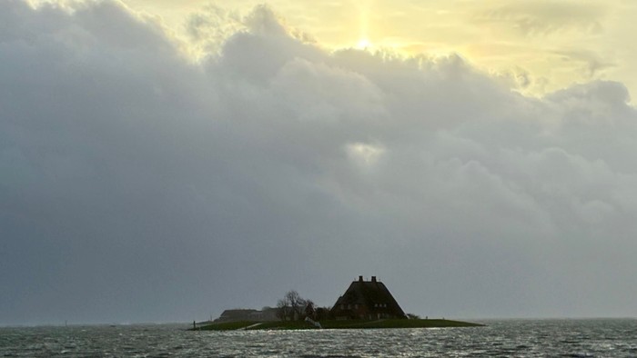 Ein einsames Inselhaus steht als Silhouette vor dramatischem, düsterem Himmel und unruhigem Gewässer.