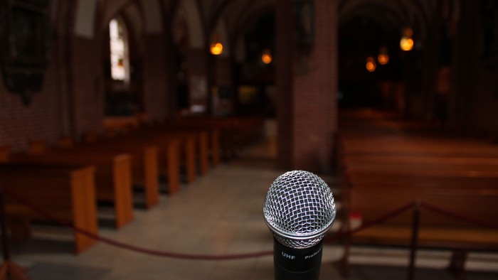 Ein Mikrofon steht in einer leeren Kirche mit Holzbänken und Bogenfenstern.