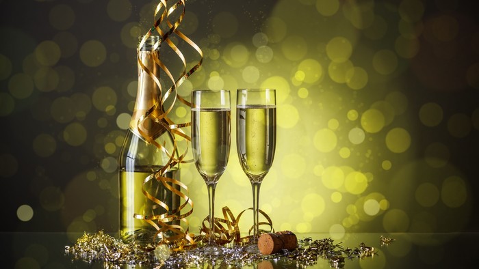 To skålene og flaske med champagnet, pyntet med guldfarvet konfetti og bælter, foran glitrende baggrund