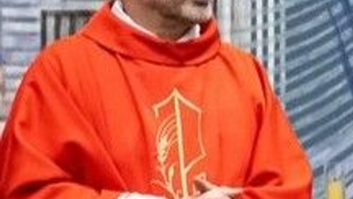 Ein Priester in roten und weißen Gewändern steht in einem Innenraum.