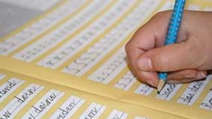 Ein Kind schreibt Buchstaben auf ein gelbes liniertes Arbeitsblatt mit einem blauen Bleistift.