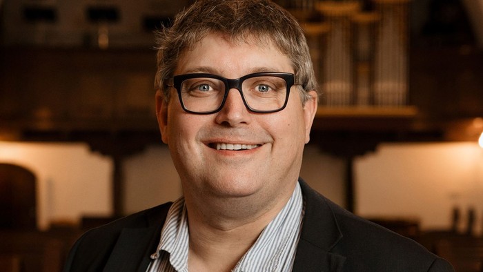 Mand med briller og jakkesæt, der smiler.