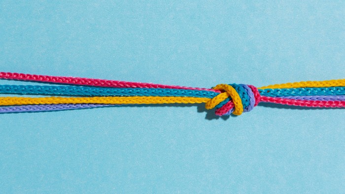 Bunte geflochtene Schnur, zu einem einfachen Knoten gebunden, vor einem hellblauen Hintergrund.