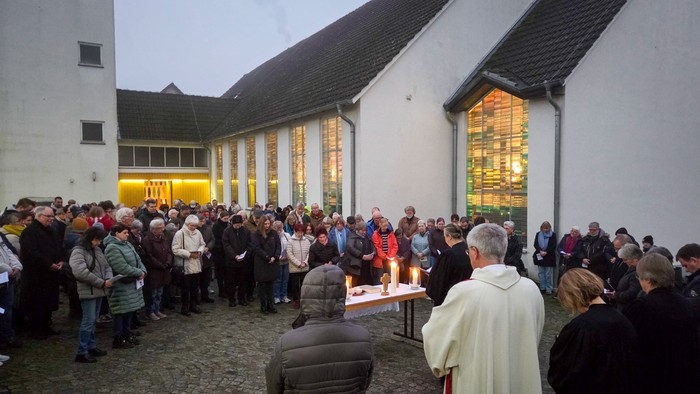 Eine Menschenmenge steht vor einer hell erleuchteten Kirche. Im Vordergrund stehen Pfarrpersonen vor einem Tisch mit Kerzen.