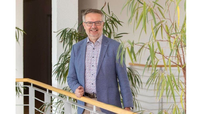 Mann in blauer Jacke lehnt an Geländer vor Grünpflanzen