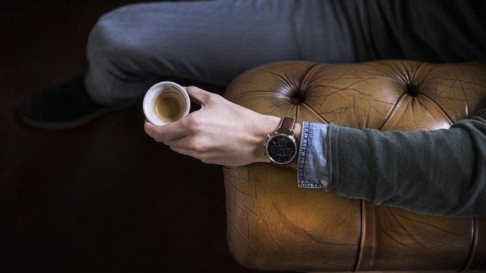 En person sidder på en brune læderstol og holder en kaffe.