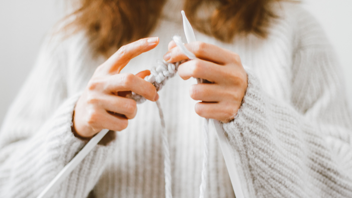 En person spinder med håndspind i hvid trøje.