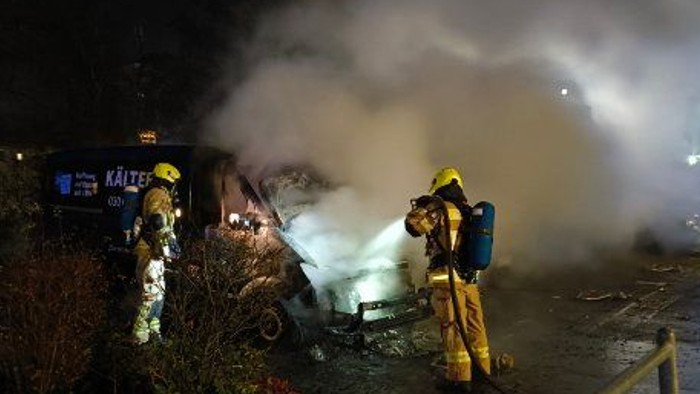 Zwei Feuerwehrleute löschen einen brennenden Bus.