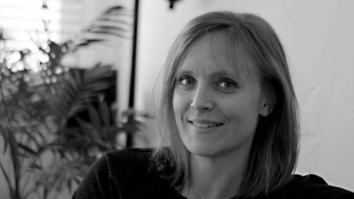 Kvinde sidder i stue med lampen bagved hende.