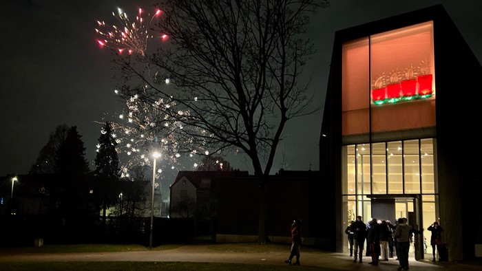Eine Gruppe Menschen steht vor dem erleuchteten Eingang der Immanuel-Kirche und betrachtet das Feuerwerk.