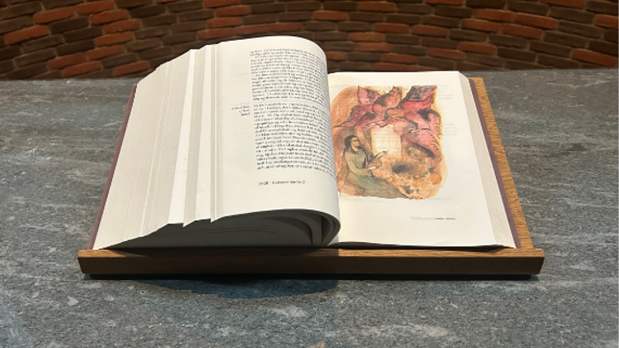 En åben bog med en sko placeret på dens sider, sat på en tekstureret overflade med et korsformet omrids.