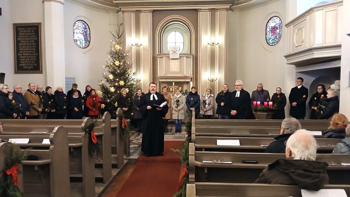 Ein festlicher Gottesdienst mit Gläubigen und Geistlichen, die sich um einen geschmückten Weihnachtsbaum versammelt haben, während einer feierlichen Weihnachtszeremonie.