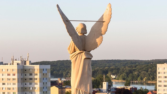 Große Engelsstatue auf hohem Sockel in Stadtlandschaft