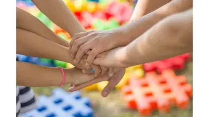 Kinderhände, die in einer Teamwork-Pose verbunden sind, mit bunten Bausteinen im Hintergrund.
