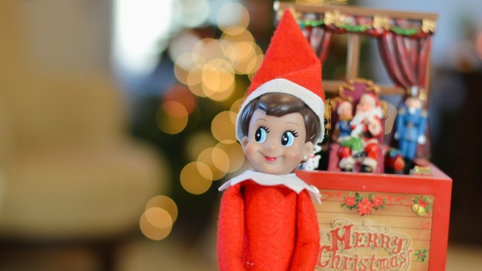 Eine Puppe mit Weihnachtsmütze neben einem Kasten mit Spielzeug vor einem verschwommenen Hintergrund