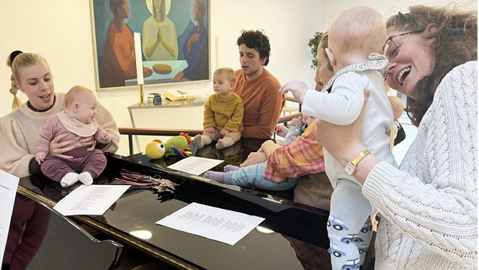 En gruppe af voksne og børn sidder om en bord og ser på en robot.