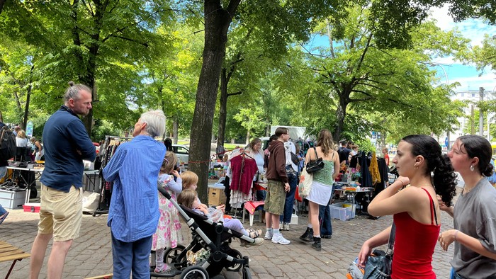 Belebter Freiluftmarkt oder Jahrmarkt mit Menschen, die unter belaubten Bäumen an Ständen stöbern.