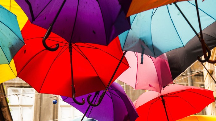Farverige paraplyer ophængt over hovedet skaber et levende, kunstnerisk baldakin mod himlen.