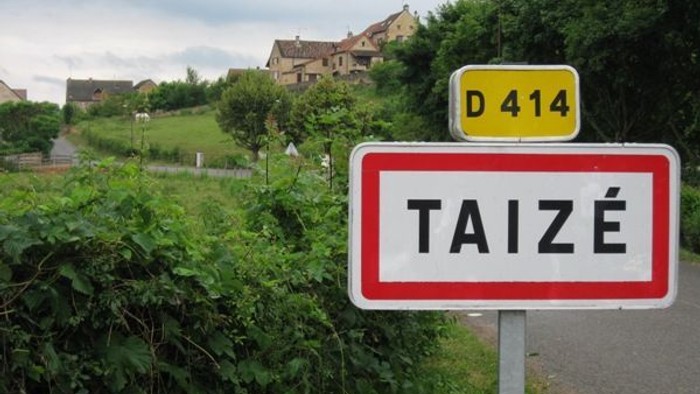 Ein Ortseingangsschild für Taizé mit einer kleinen Straße und Häusern im Hintergrund