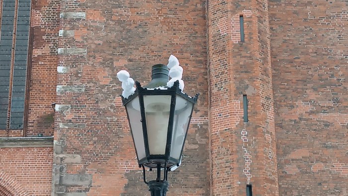 Alte Straßenlaterne, montiert an einer verwitterten Backsteinfassade mit abgenutzten Strukturen.