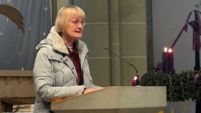 Eine Person, die auf einer Kanzel in einer Kirche spricht, umgeben von religiösen Statuen und Kerzen.