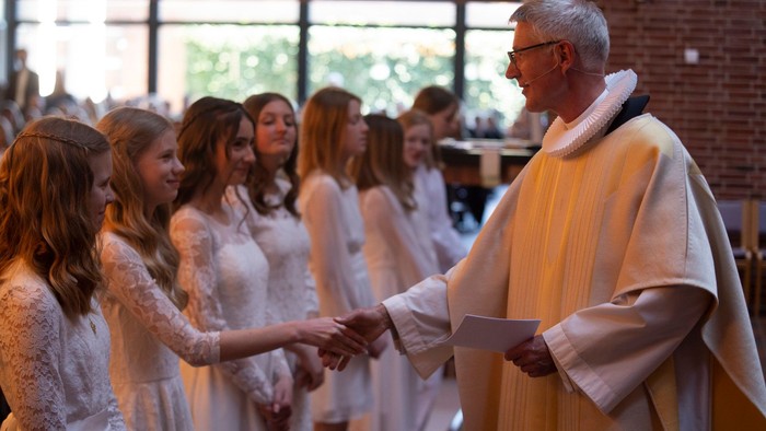 En præst skærer et barns fingre under en dåbsceremoni i en lys og rummelig lokalitet.