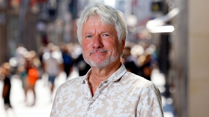 Ein älterer Mann mit grauen Haaren steht in einer belebten Stadt.