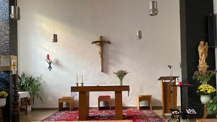 Ein ruhiger Kapelleninnenraum mit einem hölzernen Altar, einem Kruzifix, Kerzen und dekorativen Blumenarrangements.