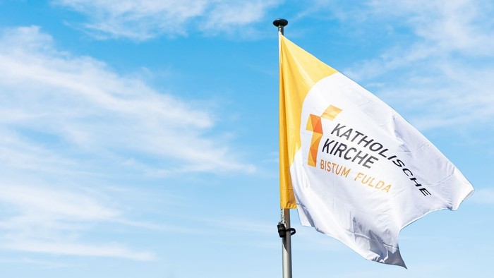 Eine gelb-weiße Flagge, die die katholische Kirche im Bistum Fulda repräsentiert, weht vor einem blauen Himmel.