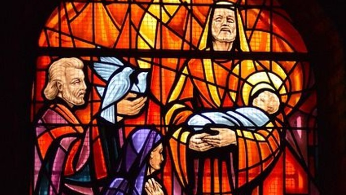 Bemaltes Glasfenster mit einer biblischen Szene, die Jesus mit Maria und einer knienden betenden Figur darstellt.