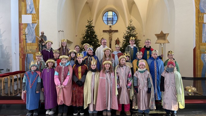 Kinder in farbenfrohen mittelalterlichen Kostümen posieren gemeinsam in einer Kirche während einer festlichen Feier.