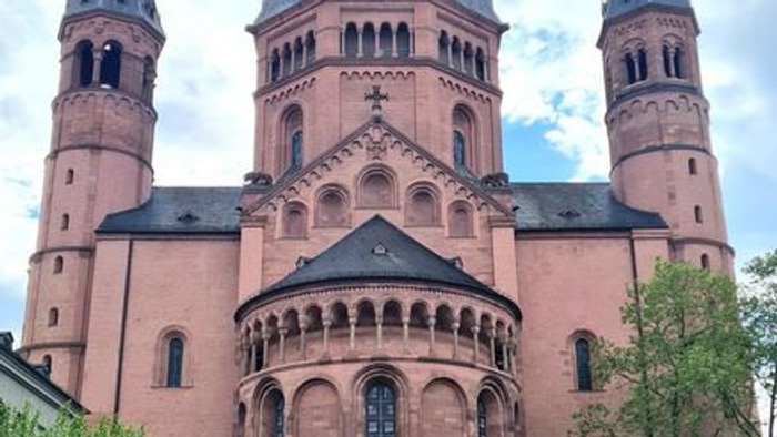 Historische romanische Kathedrale mit Zwillingstürmen und filigranem Steinwerk unter einem teilweise bewölkten Himmel.