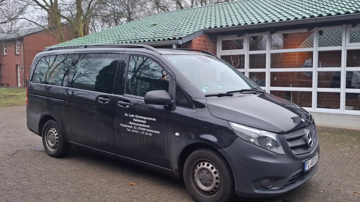 Ein schwarzer Mercedes-Transporter parkte vor einem Gebäude mit grünen Dachziegeln und Backsteinmauern.
