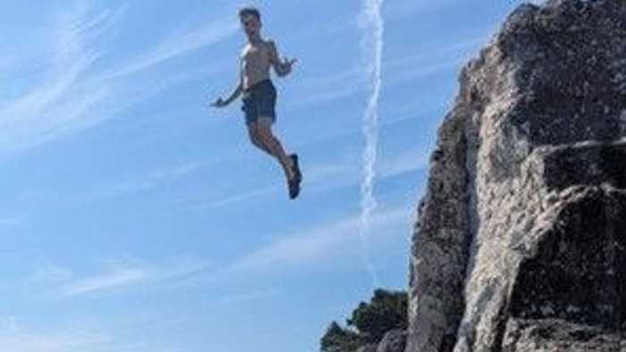 Eine Person, die mitten in der Luft von einer hohen, felsigen Klippe in den klaren blauen Himmel springt.