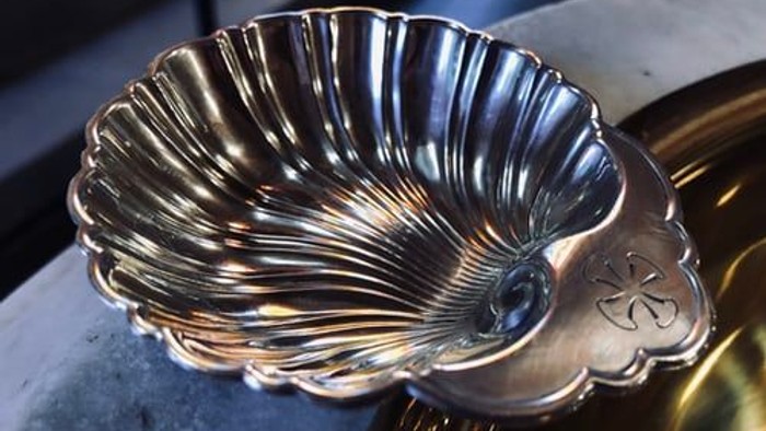 Silver shell-shaped object with intricate design on a golden surface.