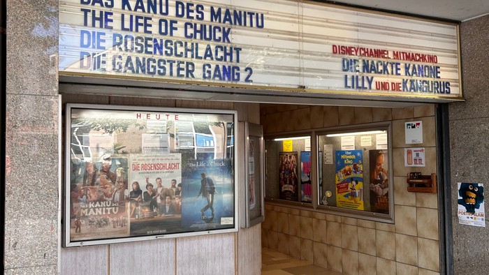 Es ist ein Kinoeingang zu sehen mit Hinweisen der aktuell laufenden Filme.