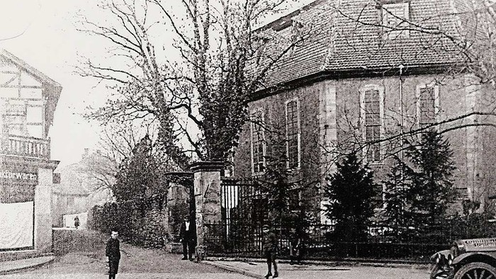 Vintage-Straßenszene mit Architektur aus dem frühen 20. Jahrhundert, kahlen Bäumen und einigen Fußgängern sowie einem alten Auto.