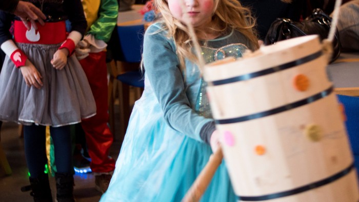 En pige i blå kagekostume slår på en tromme.