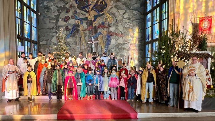 Eine vielfältige Gruppe von Kindern und Geistlichen nimmt an einer festlichen Kirchenprozession mit farbenfrohen Kostümen und religiösen Dekorationen teil.