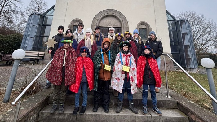Gruppe in farbenfroher traditioneller Kleidung, die vor einer kleinen Kirche auf Treppen posiert.