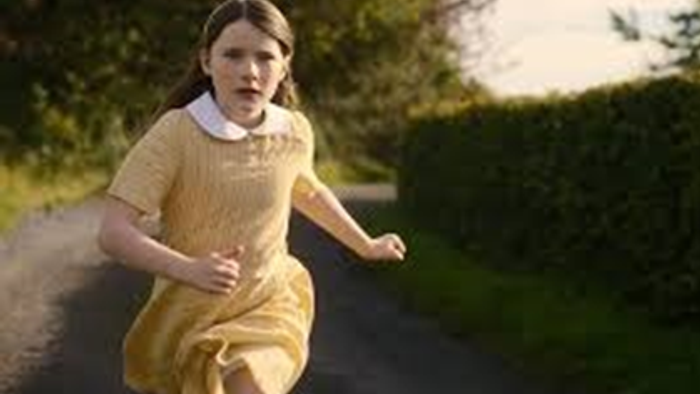 Unge pige i en gul kjole løber energisk ned ad en landlig sti.