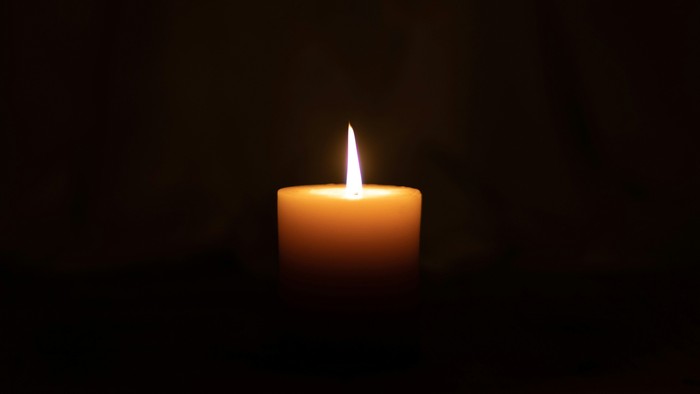 Eine einzelne brennende Kerze, die sanft vor dunklem Hintergrund leuchtet.