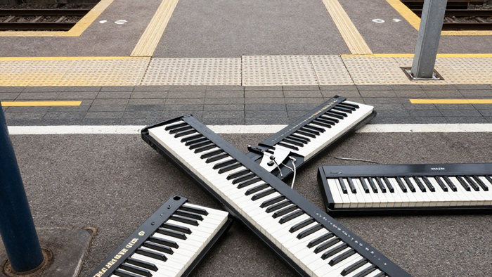 Zwei tragbare Keyboards, die sich auf einem Bahnsteigpflaster kreuzen.